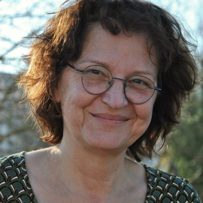 Ute Trappmann-Sowa Eine Frau, mit runder Brille und halblangen braunen Haaren, lächelt in die Kamera.